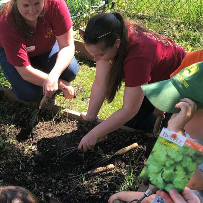 ISU Extension and Outreach Rising Star interns Tatum Kahler and Maelyn Thome working in a garden with rural Iowa youth.