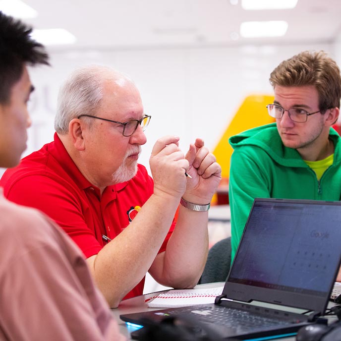 Instructor Jim Heise talks with students in his mechanical engineering capstone course.