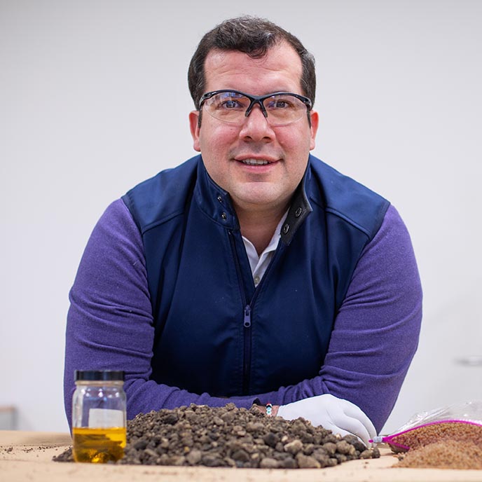 Nacu Hernandez poses with components of his asphalt - modified soybean oil, milled asphalt and soybean oil based polymer.
